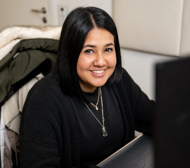 Eine Kanzlei-Mitarbeiterin blickt freundlich in die Kamera und bearbeitet die Fälle der Mandanten am Computer.