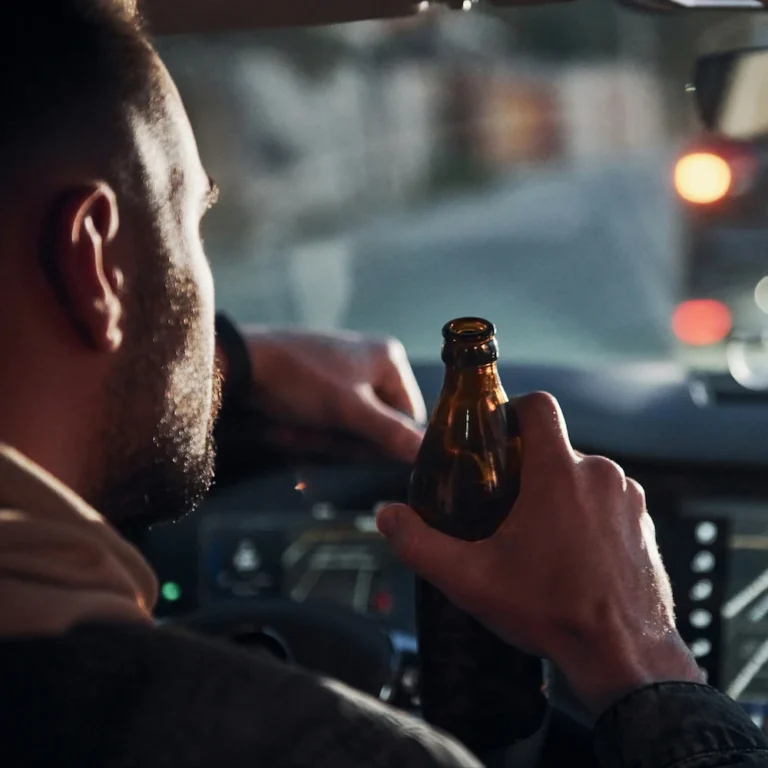 Mann fährt Auto und hält eine Bierflasche in der Hand