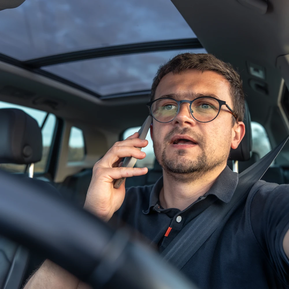Mann begeht Verkehrsordnungswidrigkeit da er Handy am Ohr hat und telefoniert, während er Auto fährt